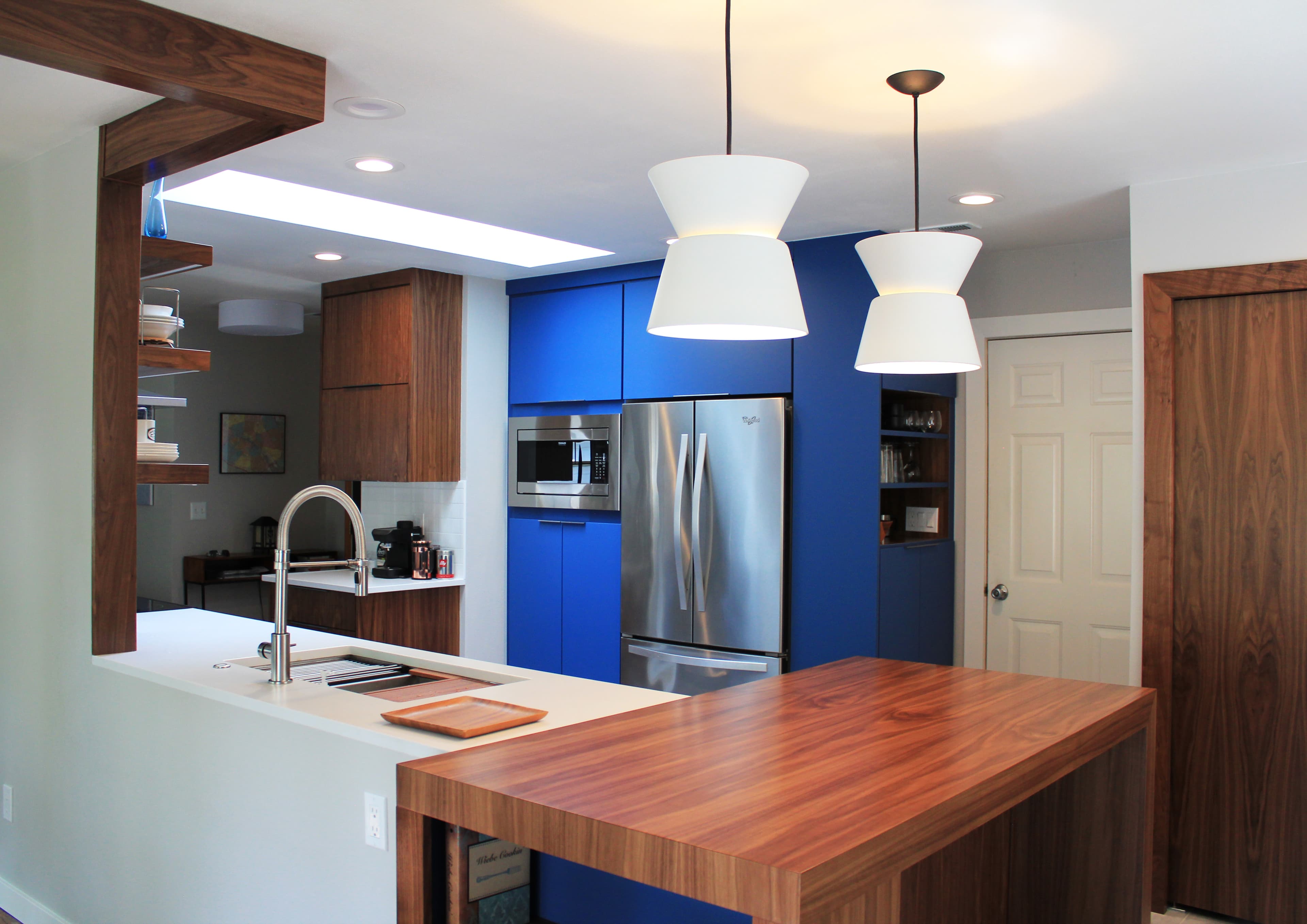 Modern kitchen with blue cabinetry, stainless steel appliances, a wood island, and white pendant lighting.